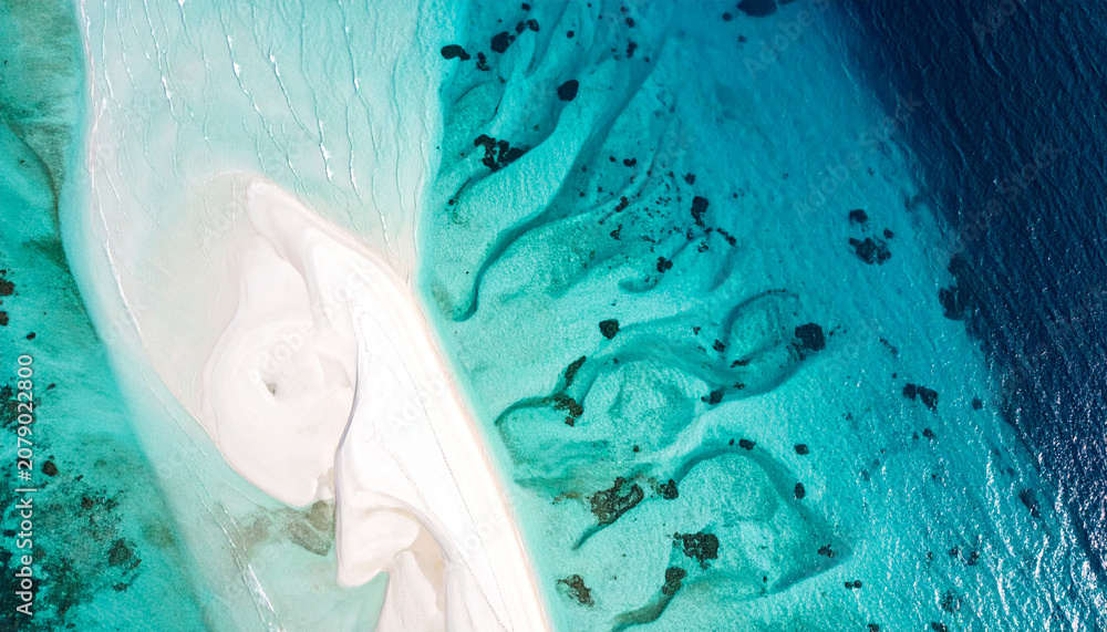 Fototapeta premium Abstrakte Luftaufnahme von oben auf ein flaches tropisches Riff mit einer Sandbank, sanfte Wasserrippeln über kreideweißen und aquamarinfarbenen Strukturen, helles Design