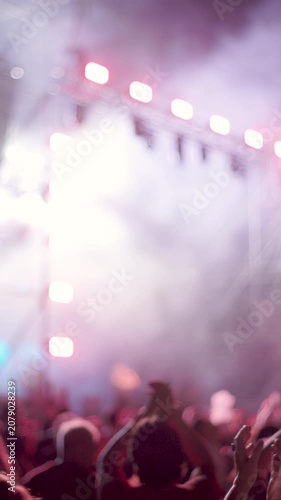 vertical shot. A crowd of people is dancing and cheering at a live music concert. Bright, multicolored stage lights illuminate the audience. An energetic atmosphere and a thrilling live performance.