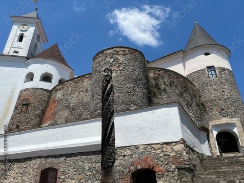 Quadro su tela Low angle view of medieval castle clock tower and round stone bastions with carved wooden totem pole against blue sky with clouds