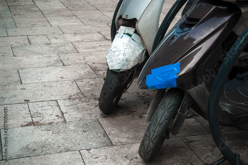 Canvas-taulu Two damaged motor scooters repaired with duct tape parked on a city pavement