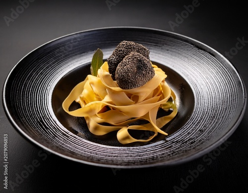 fresh tagliatelle pasta nest with shaved black truffle on dark ceramic plate against black background fine dining