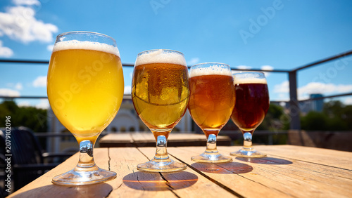 Craft beer tasting flight on sunny terrace table with blue sky background. Concept of brewery menu  outdoor bar promotion  seasonal drink advertising  beverage branding and beer tasting experiences.
