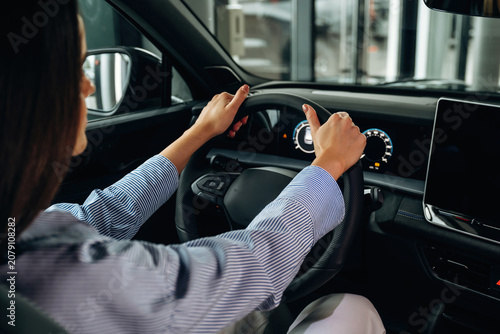 Bilde på lerret Female driver with long dark hair grips steering wheel inside modern car, dashbo