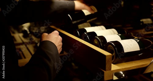 Close-up of a person selecting and pulling out a bottle of red wine from a modern wooden cellar rack