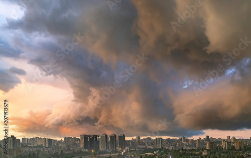 Clouds form over city skyline during sunset with shades of orange, pink, and purple in the sky