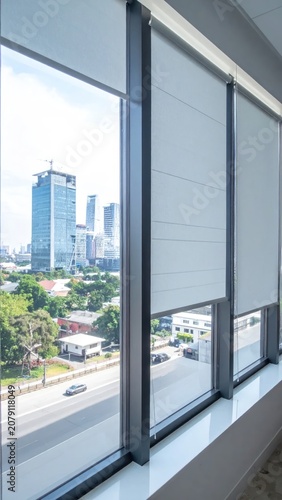 Interior view of modern office window with city skyline through a roller blind