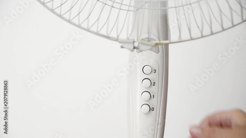 Female hand presses the power button to switch on an electric pedestal fan at home. Close-up of starting a household fan for cooling, ventilation and comfort during hot summer weather.