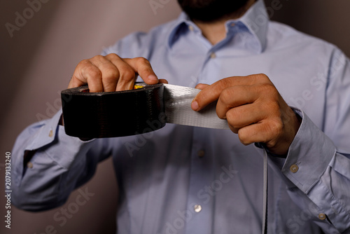 Φωτογραφία Close up of man's hands unrolling strong black duct tape for repairs or crafts