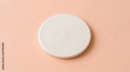 A single round minimalist white ceramic plate or coaster isolated on a smooth peach-colored background, showcasing clean lines and elegant simplicity.