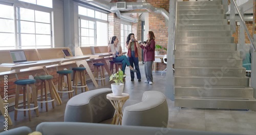 Diverse coworkers gathering around peer showing phone, holding cups on break in lounge, office wear