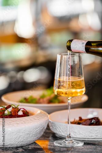 Cuadro en lienzo White wine pouring into a crystal glass on a restaurant table with gourmet food plates, close-up