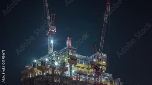 Illuminated construction cranes high angle night timelapse filmed across Dubai. The exposed structural framework of the new tower glows brightly against the dark sky. Massive scale.