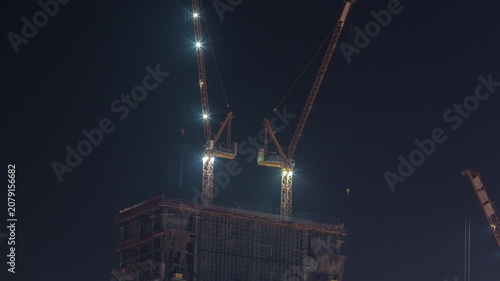 Tower crane floodlights overhead timelapse sequence captured clearly above Dubai. The towering crane structures are barely visible against the completely black night sky.