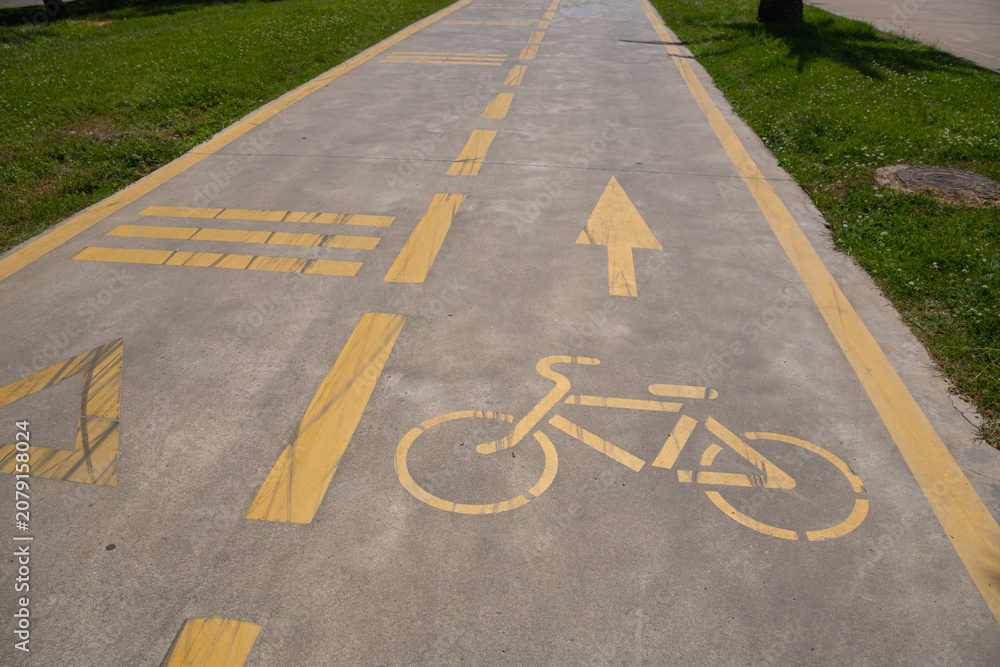 Obraz premium Concrete path featuring yellow painted road markings, including a bicycle symbol, directional arrow, and horizontal lines, defining a dedicated cycling lane
