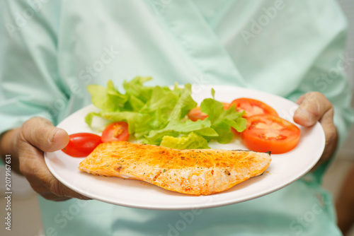 Asian elderly woman patient eating salmon stake and vegetable salad for healthy food in hospital.