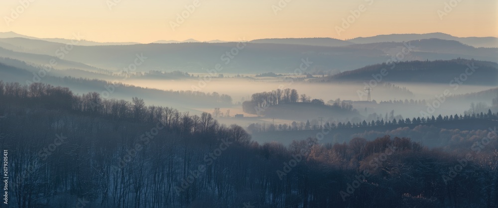 Fototapeta premium Misty spring morning with soft snow highlights and broad valley view for copy space