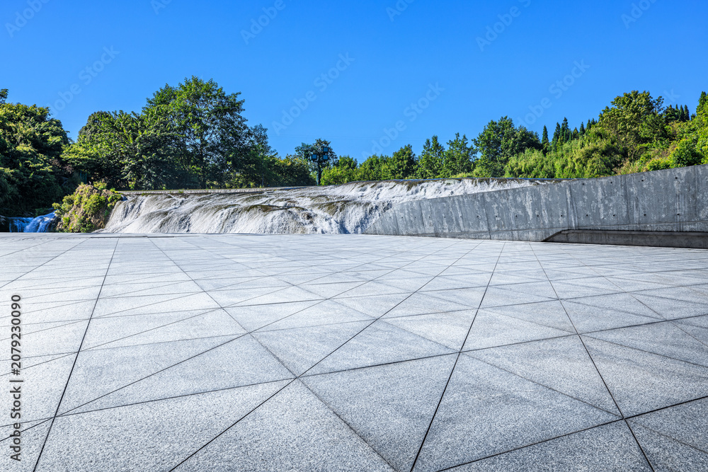 Naklejka premium Empty plaza and cascading waterfall under clear blue sky in Guizhou, China