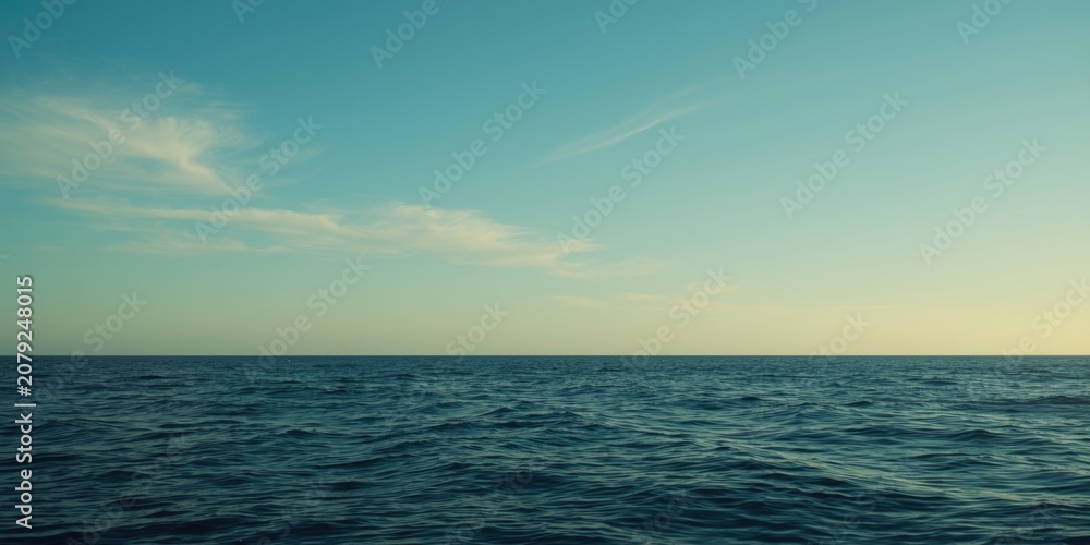 Fototapeta premium Tranquil ocean scene featuring a clear blue sky and soft wispy clouds on the horizon