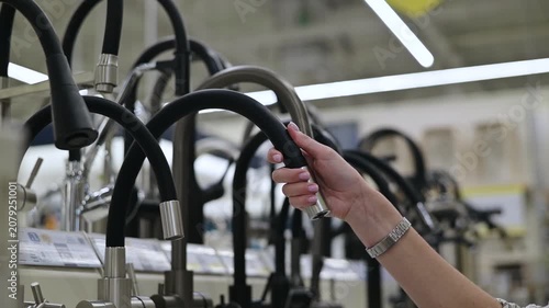 A person is seen interacting with different faucet designs displayed in a kitchen supply store. The activity involves reaching for and testing the faucet handles in a contemporary setting