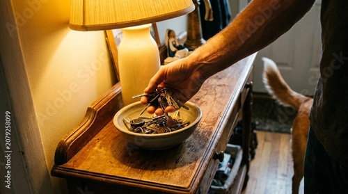 Man holding keys in bowl on wooden table with hand lamp dog