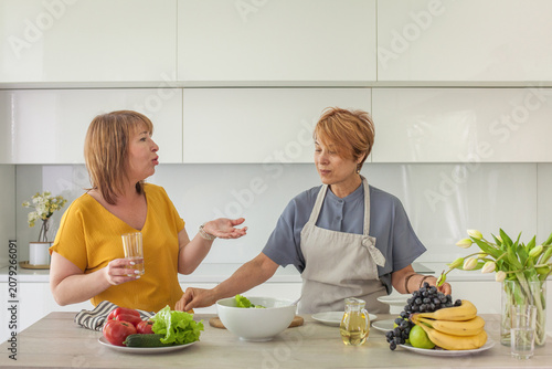 Mid adult women chatting beside counter in modern kitchen lifestyle portrait