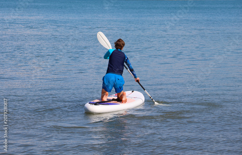 young men  riding  on sup surfing in the sea at sunset