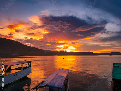Vibrant sunset over Riung Bay and the 17 Islands Marine National Park, Flores, Indonesia, with traditional boats on calm water beneath dramatic orange, gold, and purple clouds