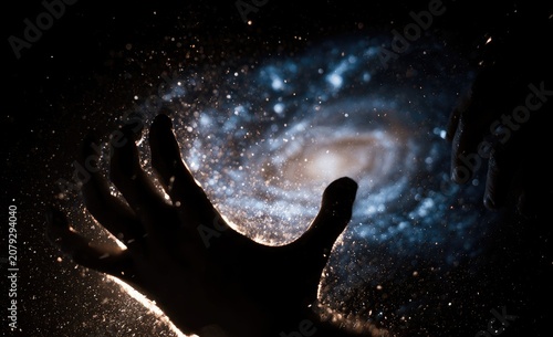 Human Hand Reaching Towards a Swirling Galaxy in Space.