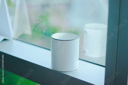 Minimal white ceramic mug mockup placed on a windowsill with soft natural light and a blurred background. Perfect for branding, logo presentations, product showcases, coffee shops, and e-commerce list