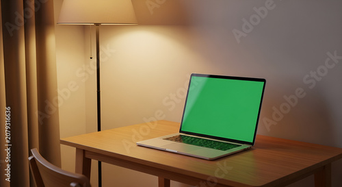 Laptop with green screen on wooden desk in a cozy room with warm lamp light