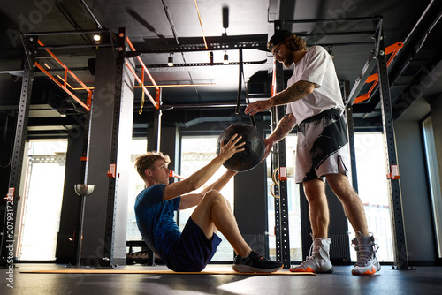 Bild auf Leinwand Personal trainer handing medicine ball to young athlete during core workout