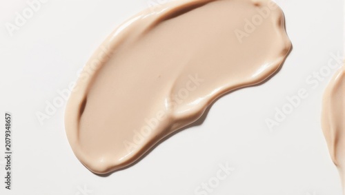 Swirl of light beige cosmetic cream on a white surface, smooth and textured