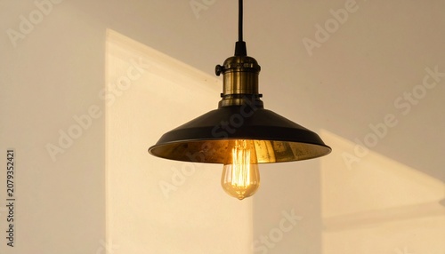 A single hanging pendant light fixture with black ceiling mount, cord, and brass socket holding an exposed Edison bulb, minimalist industrial design glowing warmly against a neutral background.