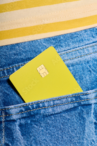 Closeup of a yellow debit card with a microchip sticking out of the back pocket of a pair of jeans.