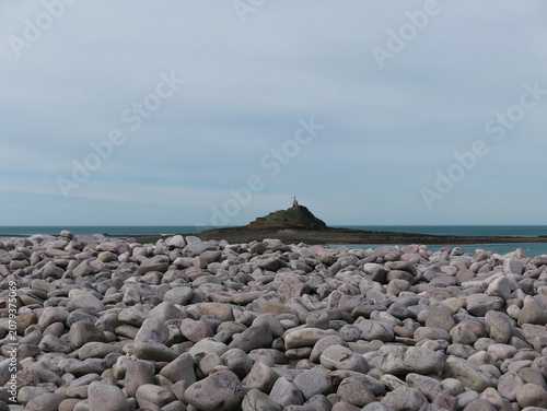 remote and hazy view of Mont Saint Michel as a backdrop to a pebble beach