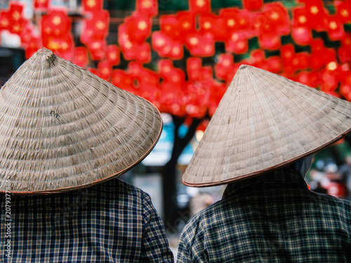Fotografie Two Vietnamese people wearing traditional conical hats seen from behind with vibrant red bokeh background