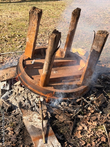 Close-up of an old table burning on a fire pit outdoors in a natural setting with smoke rising around it.