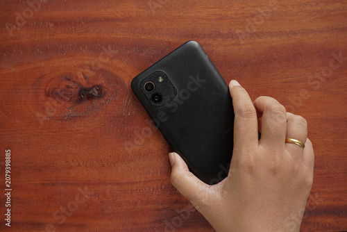 Photos Hand holding a smartphone face down on a wooden table