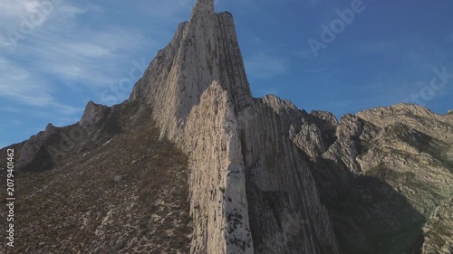 Majestic rocky mountain peaks filmed from aerial perspective with clear blue sky backdrop, camera slowly rotating around dramatic geological formations highlighting natural grandeur