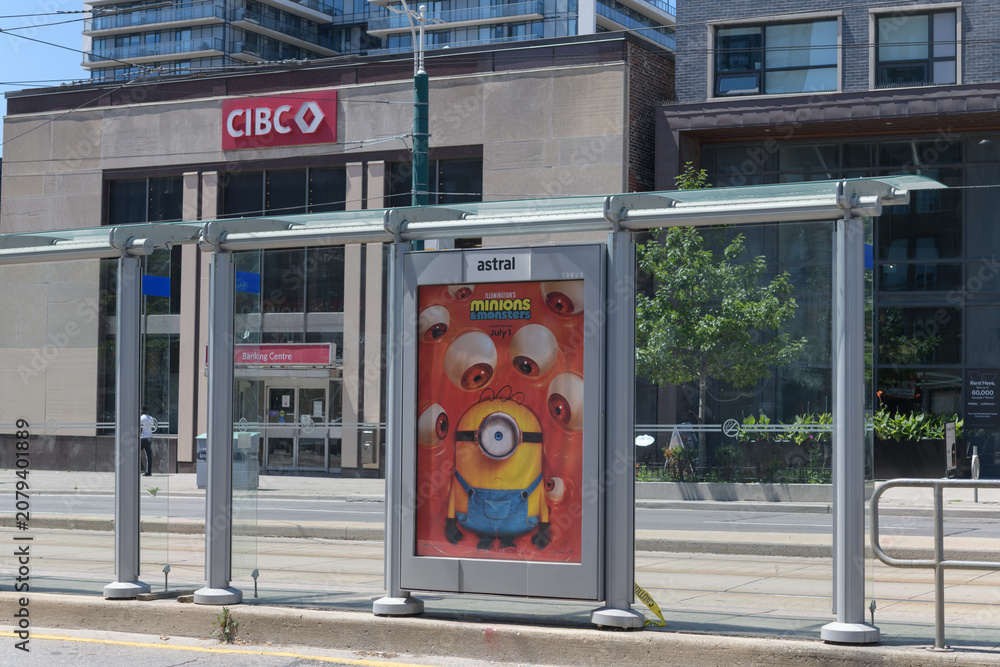 Obraz premium transit shelter OOH advertising featuring Minions & Monsters animation and defocused view of CIBC bank branch at 268 College St, Toronto
