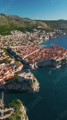 Epic Dubrovnik old town ancient castle architecture vertical aerial panorama. 
Cinematic drone panning flight of Lovrijenac fortress, medieval stone walls, 
terracotta roof tiles and blue Adriatic sea