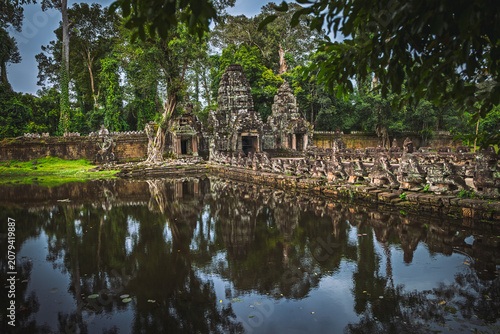 View of the ancient stone ruins of Preah Khan temple surrounded by lush jungle trees and a reflective moat with stone statues in Krong Siem Reap, Siem Reap Province, Cambodia.