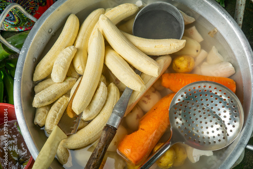 Tableau sur toile Top view of peeled green plantains carrots and potatoes soaking in a large metal