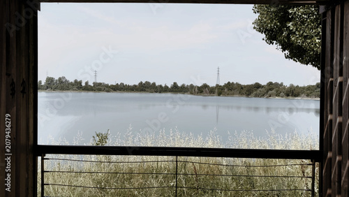 Scenic view of a calm lake and distant trees framed through a dark rectangular open structure