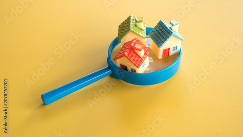Three colorful miniature model houses with red green and blue roofs sitting inside the rim of a blue magnifying glass on yellow.