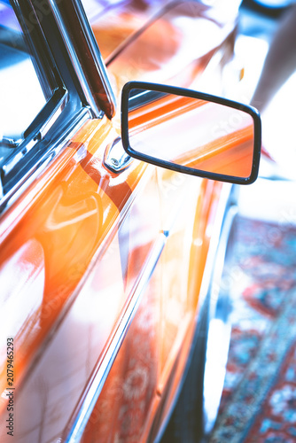 Small side rear view mirror on a bright orange vintage retro car body
