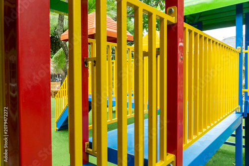 Close-up of a colorful outdoor children playground structure featuring vibrant yellow railings, red support posts, blue platforms, and a small tower with an orange roof.