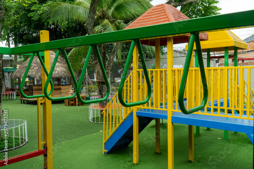 Photography Colorful children playground with green monkey bars, yellow climbing structures and artificial grass in an outdoor recreational area during a bright day