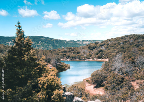 Bild auf Leinwand Vista panorámica de un lago azul rodeado de colinas boscosas bajo un cielo nubla