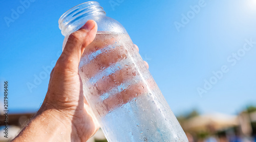 cold reusable bottle summer heat hydration outdoor water condensation hand showing a frosty drink container against blue sky for eco lifestyle branding travel safety and heat relief themes